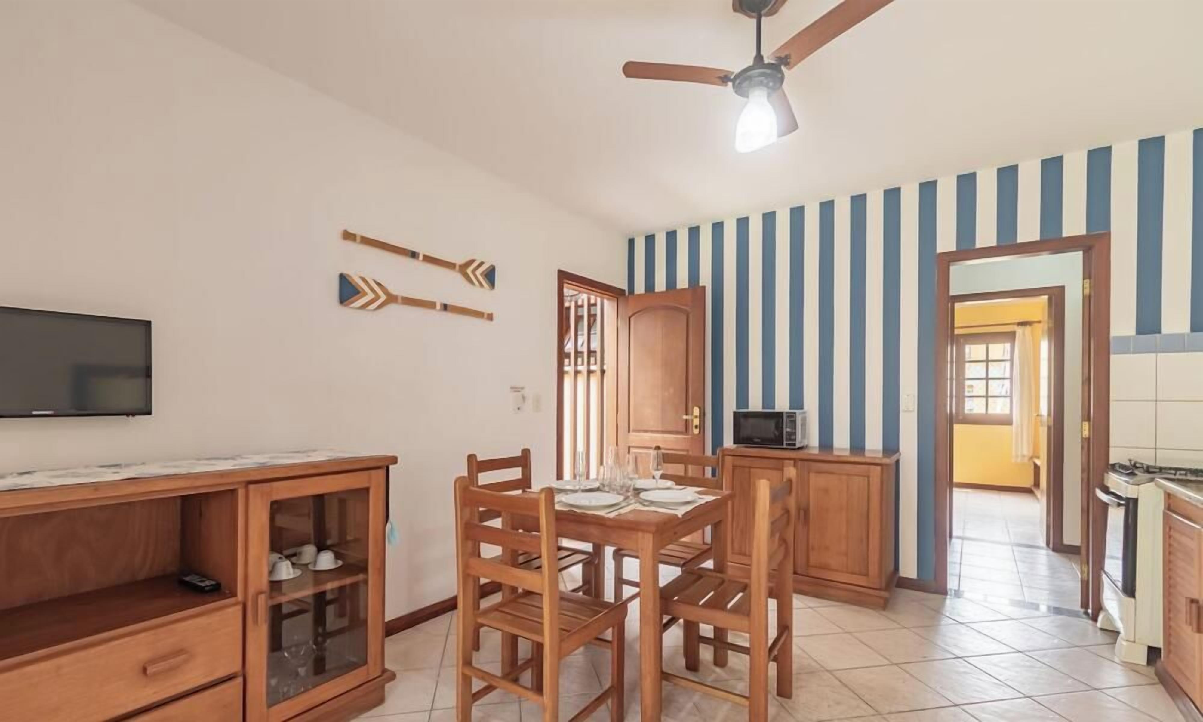 A dining area with a wooden table and chairs, a television on the wall, and a ceiling fan.