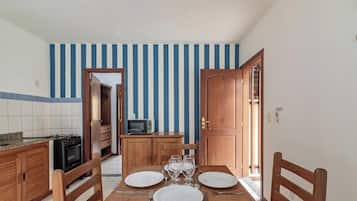 A compact kitchen with a microwave, stove, and wooden cabinets. A dining table with chairs and a small cabinet is in the center.