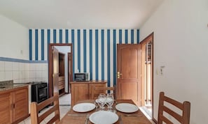 A dining area with a wooden table set for four, a kitchen with a stove and microwave, and a striped wall. - Comfortable Apartment Beachfront Condo Jso0007 (Porto Seguro)