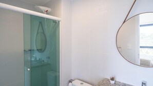 A modern bathroom with a glass shower enclosure, a toilet, a sink with a granite countertop, and a large mirror. - Apartment With Pool in Barra - Salvador Blb1004 (Salvador)