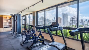 Una palestra con attrezzature per esercizi, ampie finestre e vista sulla città.
