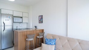 A compact kitchen with a refrigerator, microwave, and a wooden island with bar stools. - Apartment With Pool in Barra - Salvador Blb1004 (Salvador)