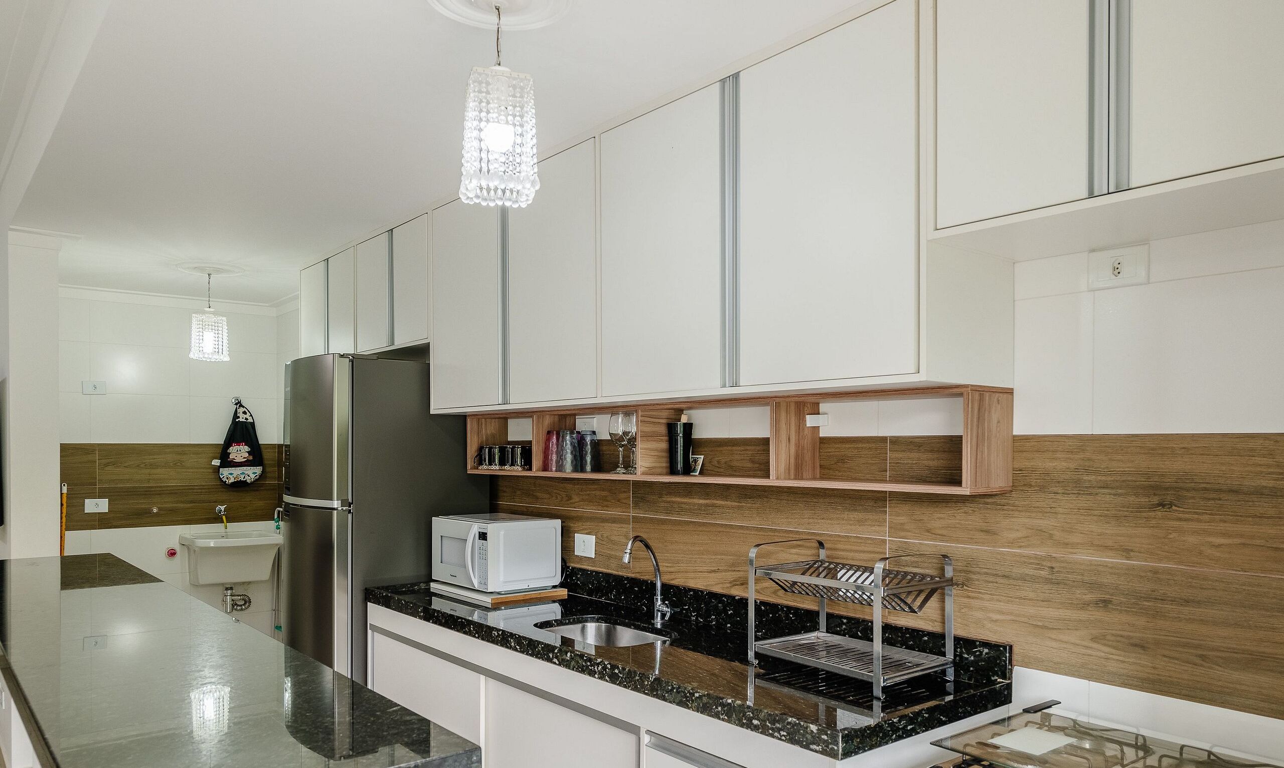 A modern kitchen with a stainless steel refrigerator, a microwave, and a sink with a metal drying rack.
