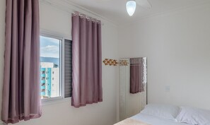 Ein Schlafzimmer mit einem Bett, einem Vorhangfenster, einem an der Wand befestigten Spiegel und einer Deckenleuchte.