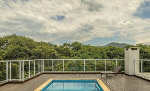 Ein Pool auf dem Dach mit einer Holzterrasse, umgeben von einer weißen Reling, mit Blick auf eine üppige grüne Landschaft mit Bäumen und fernen Bergen.