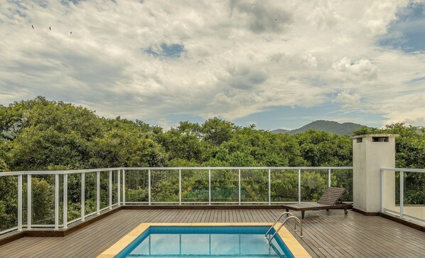 A rooftop pool with a wooden deck, surrounded by a white railing, and overlooking a lush green landscape with trees and distant mountains. - Apartment in Building With Swimming Pool Rji0046 (Ubatuba)
