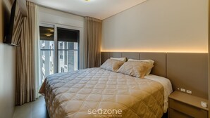 A modern hotel room with a large bed, a bedside table, and a window with curtains. - Apart w/ Barbecue in Jurere Internacional Vlo0504 (Florianópolis)