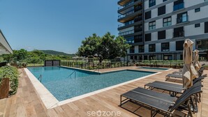 A rooftop pool area with lounge chairs and a building in the background. - Apart w/ Barbecue in Jurere Internacional Vlo0504 (Florianópolis)