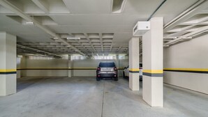 An empty parking garage with concrete floors, white walls, and yellow and black striped lines. - Apart w/ Barbecue in Jurere Internacional Vlo0504 (Florianópolis)