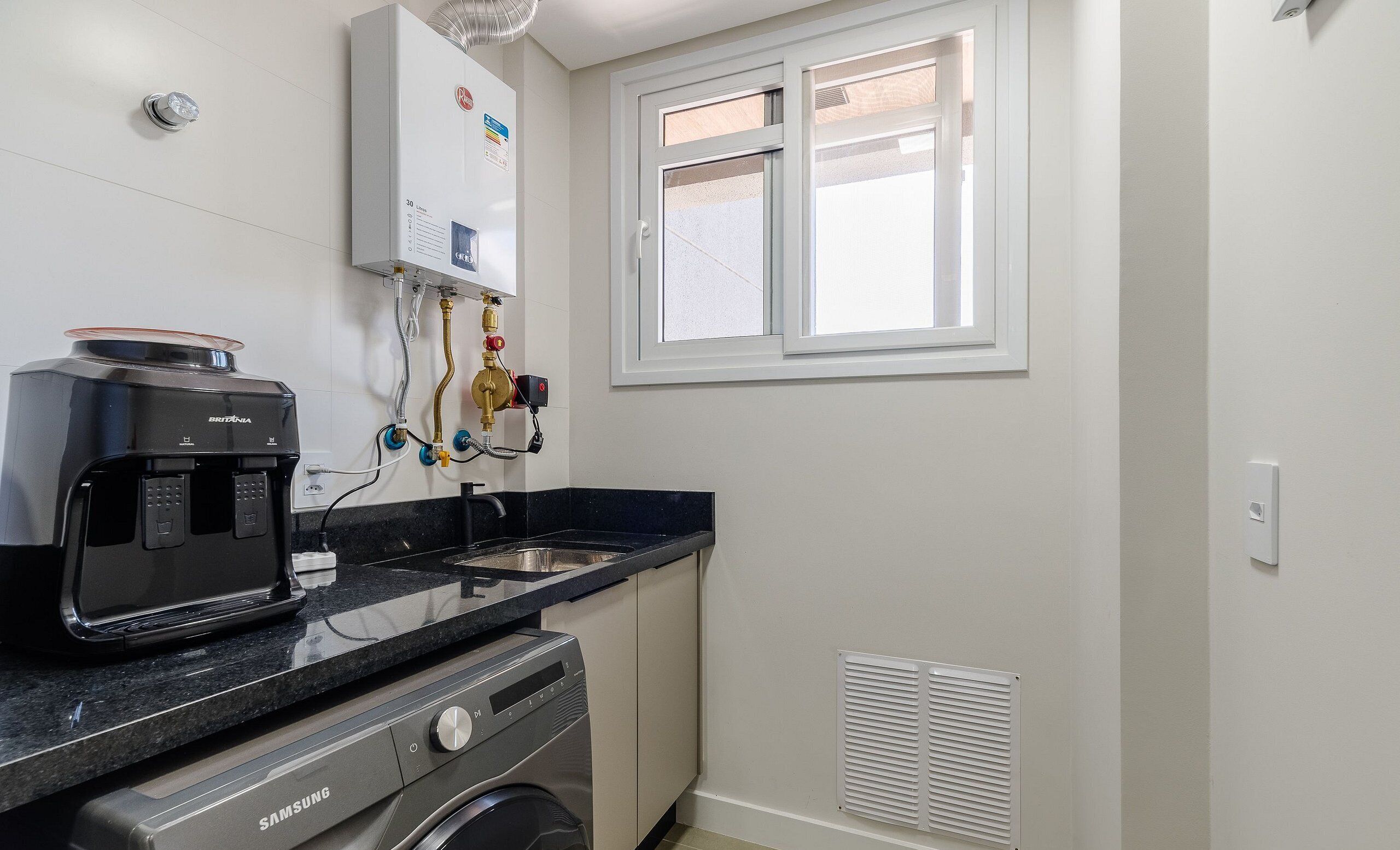 A compact kitchen with a coffee maker, washing machine, and a window with blinds.
