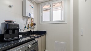 A compact kitchen with a coffee maker, washing machine, and a window with blinds. - Apart w/ Barbecue in Jurere Internacional Vlo0504 (Florianópolis)