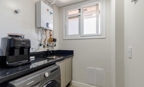 Eine kleine Küche mit Kaffeemaschine, Waschmaschine und einem Fenster mit Jalousien.