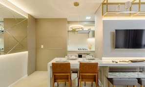 Cozinha moderna com área de jantar, apresentando uma ilha central, eletrodomésticos embutidos e uma televisão de tela plana na parede.