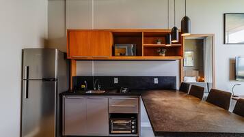 A modern kitchen with a built-in refrigerator, oven, and microwave. There is a wooden shelf above the countertop, and a dining area with a table and chairs.