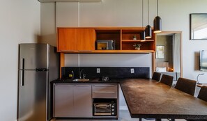 Cocina moderna con refrigerador, horno y microondas integrados. Hay un estante de madera sobre la encimera y una zona de comedor con mesa y sillas.