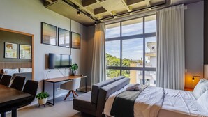 Ein modernes Hotelzimmer mit großem Fenster, einem Bett, einem Schreibtisch und einem Fernseher.
