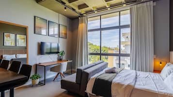A modern hotel room with a large window, a bed, a desk, and a TV.