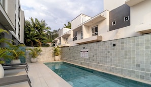 Piscina com paredes revestidas de azulejos, plantas em vasos e uma placa com texto.