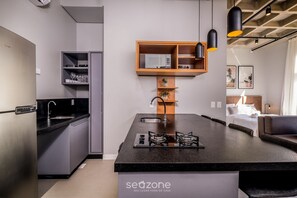 A modern kitchen with a central island, built-in shelving, and a dining area with a sofa. - Complete Loft 750m From Canas Beach Tps310 (Florianópolis)