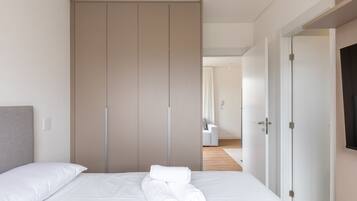 A neatly made bed with white linens and towels, a grey headboard, and a large wardrobe with sliding doors.
