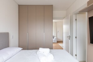 A neatly made bed with white linens and towels, a grey headboard, and a large wardrobe with sliding doors. - Functional Apt w/ Garage in Curitiba Wsh0801 (Curitiba)