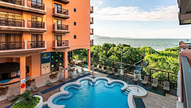 A hotel with a pool, outdoor seating, and a view of the sea. - Wonderful Suite in a Beachfront Resort Jbv108 (Florianópolis)