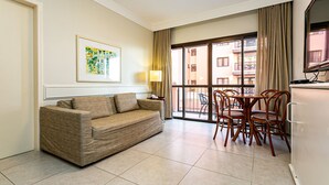 A hotel room with a sofa, dining table with chairs, a TV, a window with curtains, and a framed picture on the wall. - Wonderful Suite in a Beachfront Resort Jbv108 (Florianópolis)