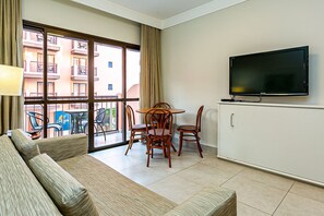 Habitació d'hotel amb un sofà, una taula de menjador i cadires, un televisor muntat a la paret i una finestra gran amb vista a l'edifici.