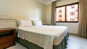 A hotel room with a bed, bedside table, and a window with curtains. - Wonderful Suite in a Beachfront Resort Jbv108 (Florianópolis)