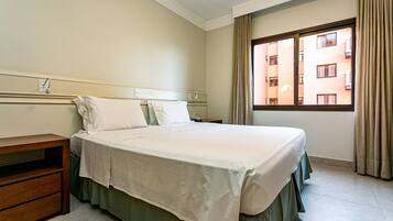 A hotel room with a bed, bedside table, and a window with curtains.