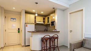 A compact kitchen with wooden cabinets, a built-in microwave, and a small island with stools. - Wonderful Suite in a Beachfront Resort Jbv108 (Florianópolis)