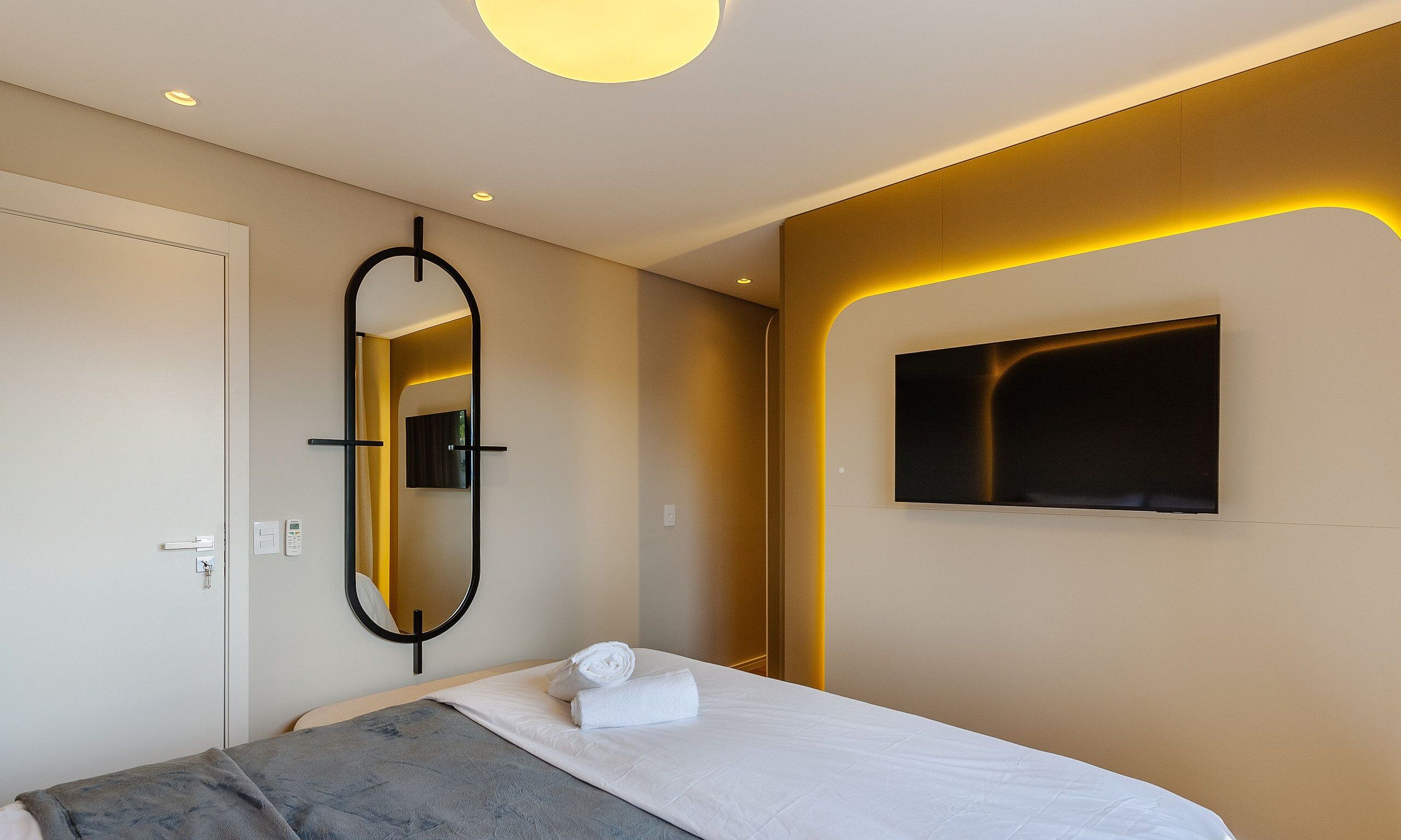 Una habitación de hotel con una cama, un espejo, un televisor fijado a la pared y una puerta.