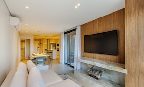 A modern living room with a large TV mounted on a wooden wall, a fireplace with logs, and a dining area with a table and chairs. - Apt in the Penthouse With Barbecue! - Dlh0501 (Gramado)