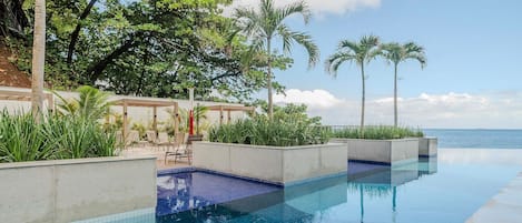 A pool area with clear blue water, surrounded by palm trees and a view of the ocean.
