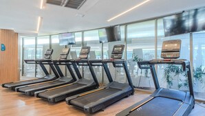 Ein Fitnessraum mit in Reih und Glied stehenden Laufbändern, großen Fenstern und einer Holzwand.