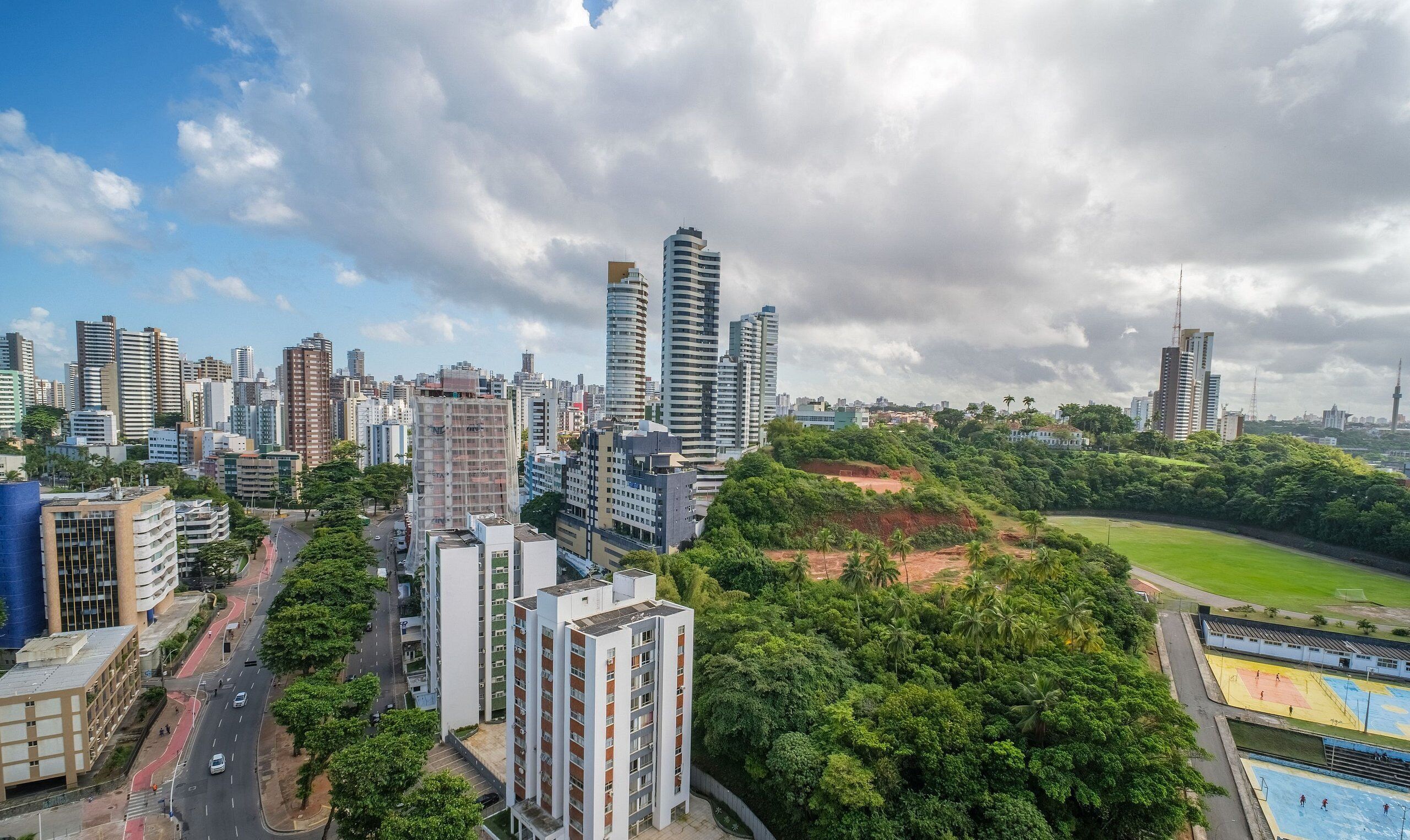 A cityscape with high-rise buildings, a green park, and a sports field.