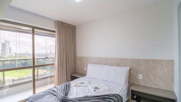 Ein Hotelzimmer mit großem Fenster, einem Bett mit weißen Leinen, einer grauen Decke und einer Marmorwand.