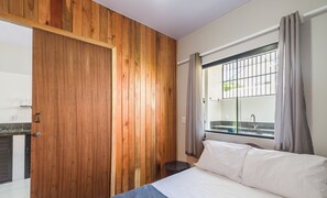 Un dormitorio con pared de madera, una cama, una ventana con cortinas y vista a un balcón.