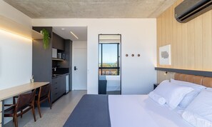 Habitació d'hotel moderna amb llit, escriptori, petita cuina i balcó amb vistes.