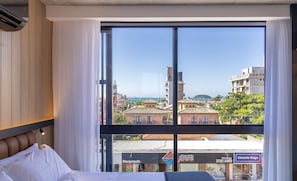 Habitació d'hotel amb una finestra gran que ofereix vistes a la ciutat i a un conjunt d'aigua.
