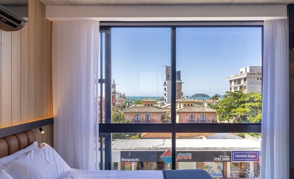 Habitación de hotel con un ventanal grande que ofrece vistas a la ciudad y una masa de agua.