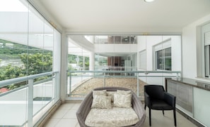 A balcony with a wicker sofa, a black chair, and a glass railing. - Apt in Resort w/ Pool 200m From the Beach Mhe0114 (Florianópolis)