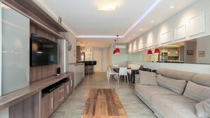 Un soggiorno moderno con televisore a schermo piatto, mobili in legno, un divano e un'area pranzo con sedie.