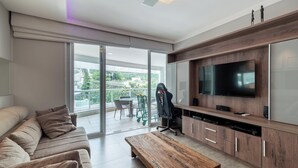 Un soggiorno moderno con una TV a schermo piatto, un divano, un tavolino da caffè e una porta scorrevole in vetro che dà su un balcone con mobili da esterno.