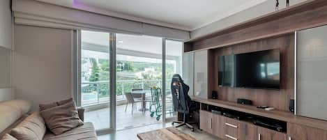 Una sala de estar moderna con un sofá, una mesa de centro de madera, un televisor y una puerta corrediza de vidrio que da a un balcón.