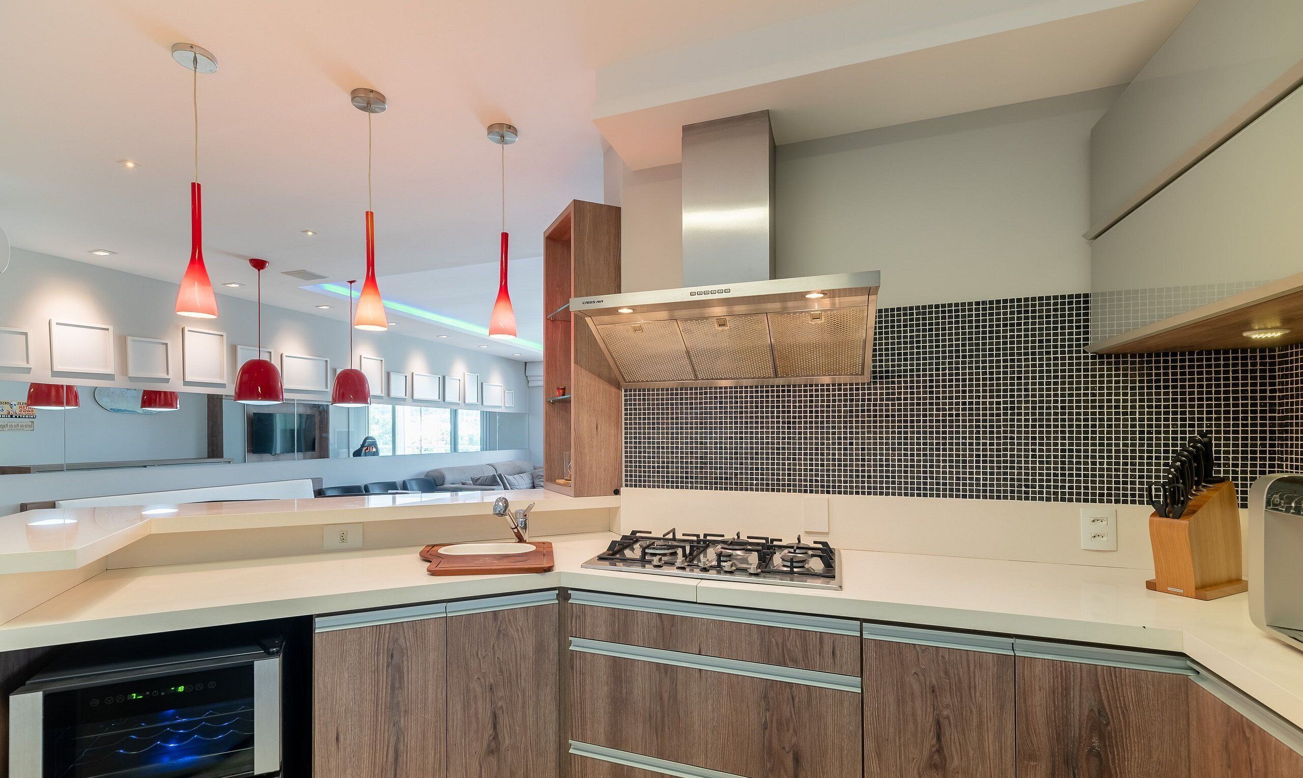 Cozinha moderna com fogão a gás, armários de madeira e luminárias pendentes vermelhas.