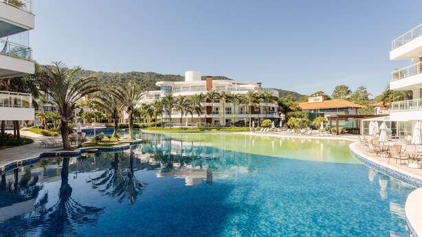 Una piscina di resort con acqua cristallina, circondata da palme e edifici moderni.