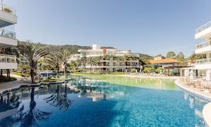 Una piscina de resort con agua azul cristalina, rodeada de palmeras y edificios modernos.