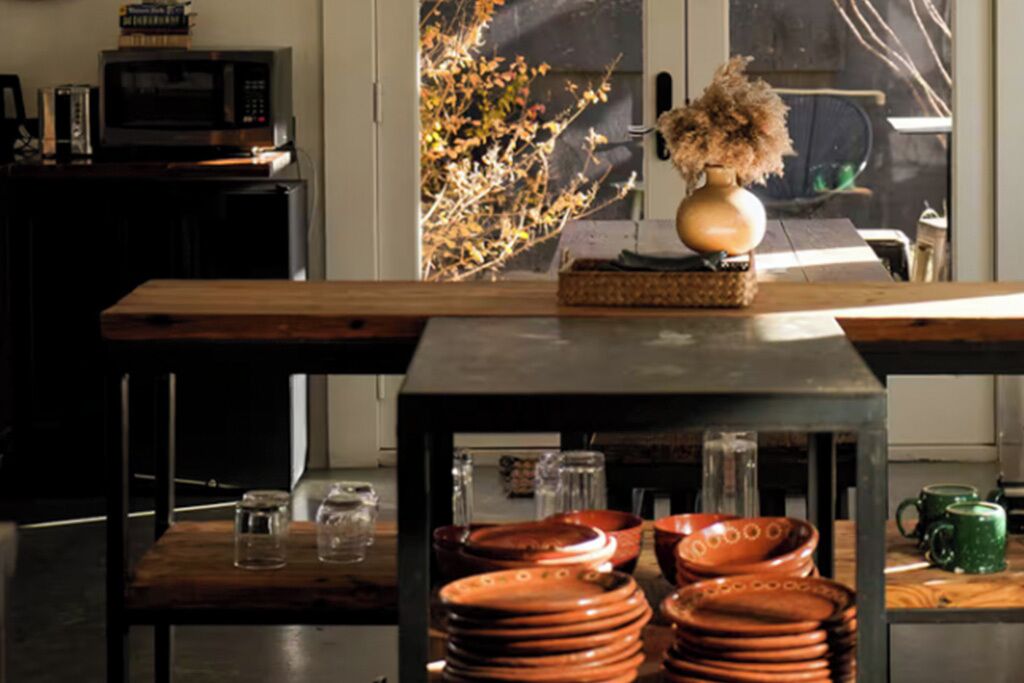 A kitchen with a wooden table, a vase with dried flowers, and a window with a view of a tree.