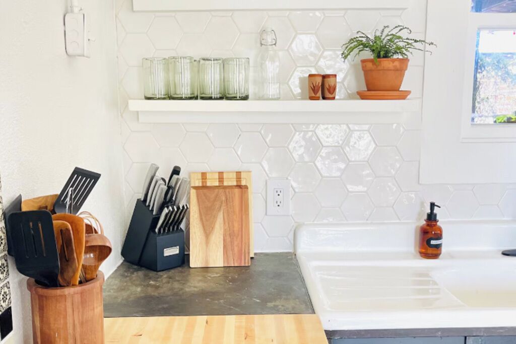 A kitchen with a countertop, a sink, a potted plant, and a hexagonal tile backsplash.